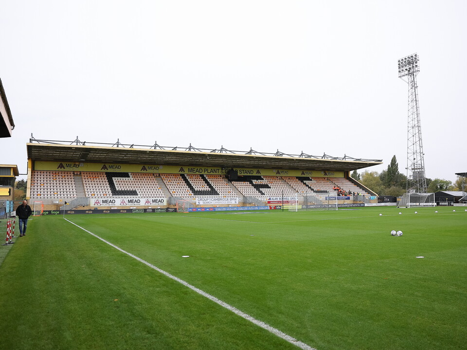 An empty football stadium with "CUF" on the upper stand and a tower behind.