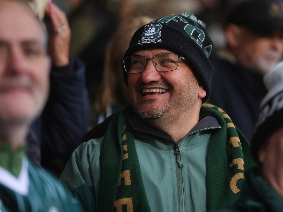 Man with glasses smiling at camera wearing green and yellow scarf and black hat