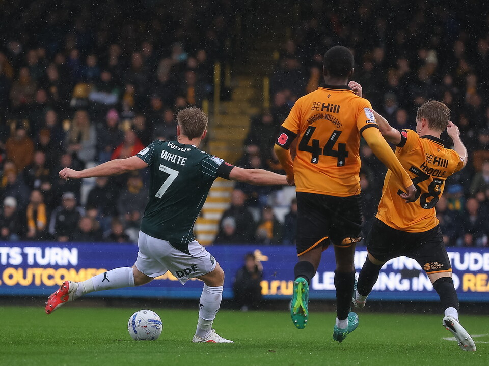 Three football players, two in yellow, one in green, battle for the ball.