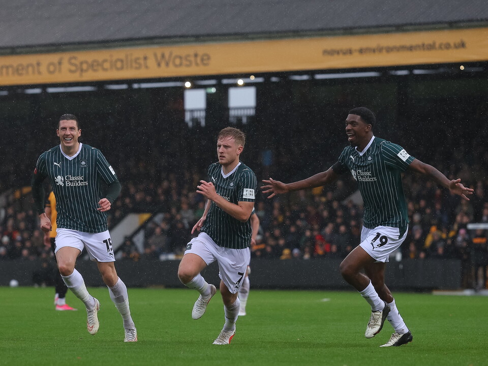 Three football players in green and white kits celebrate a goal on the pitch