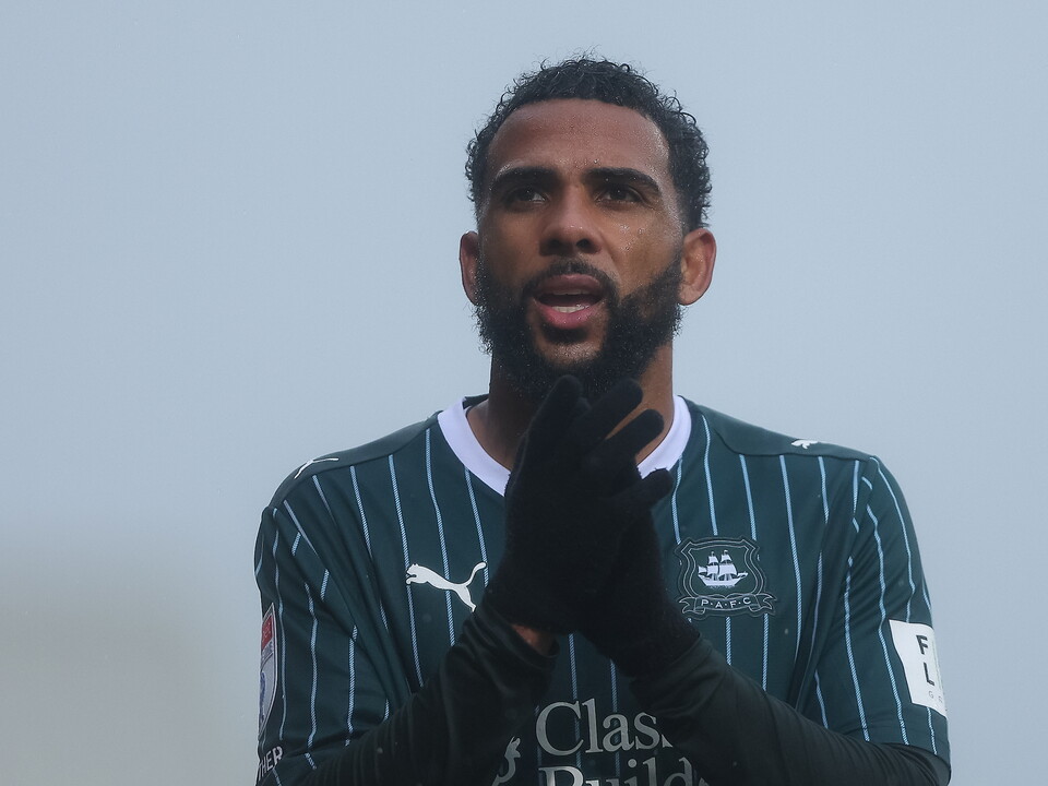 A football player wearing a black and green shirt and black gloves claps his hands