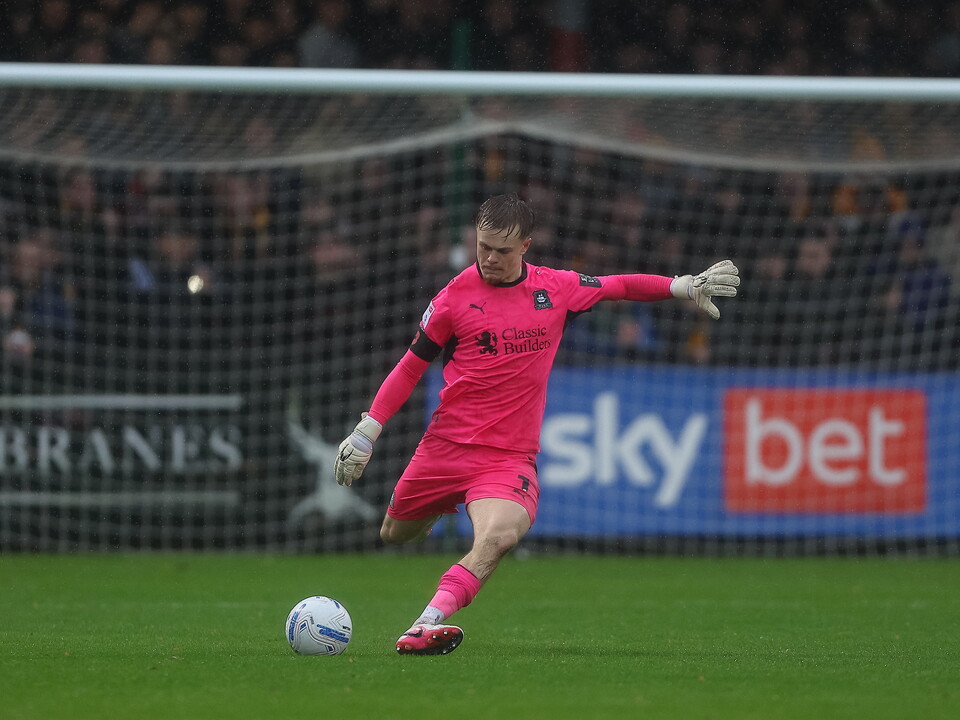 Football player kicking ball, sponsor banners behind him.