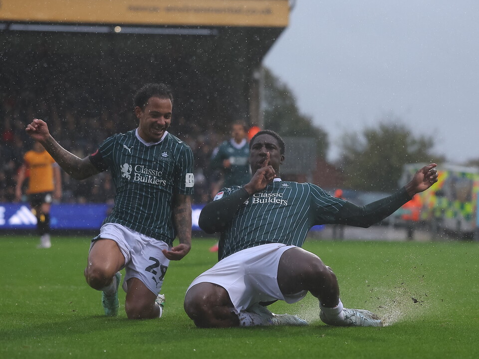 Two football players celebrating a goal in the rain on a green field.