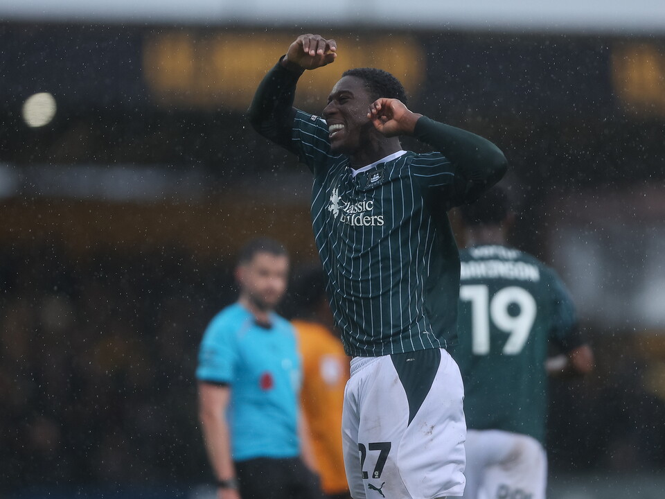 Footballer celebrates goal, hands on head, shirt number 27, rain falling, blurred background.