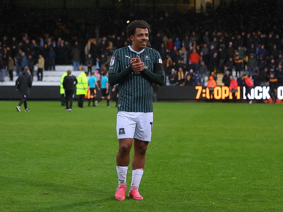 Player stands on pitch clapping hands, crowd in background, scoreboard shows 7:0.