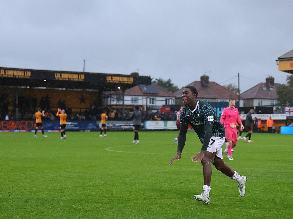 A footballer in green runs across the field with other players in the background.