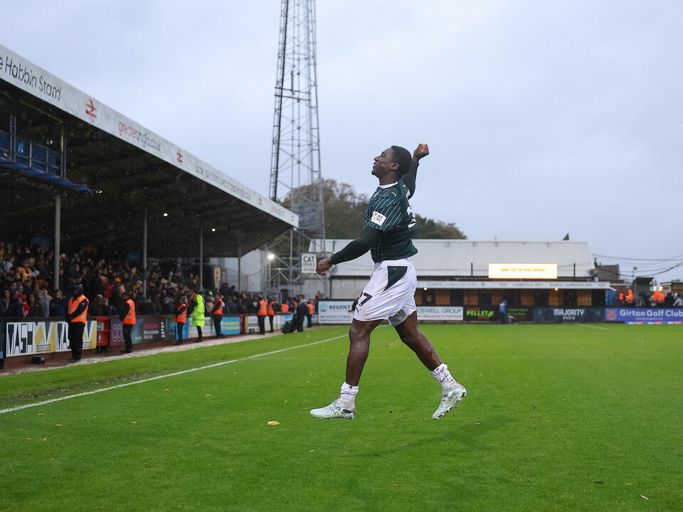Football player jumping with arms raised on a green field, stadium in the background