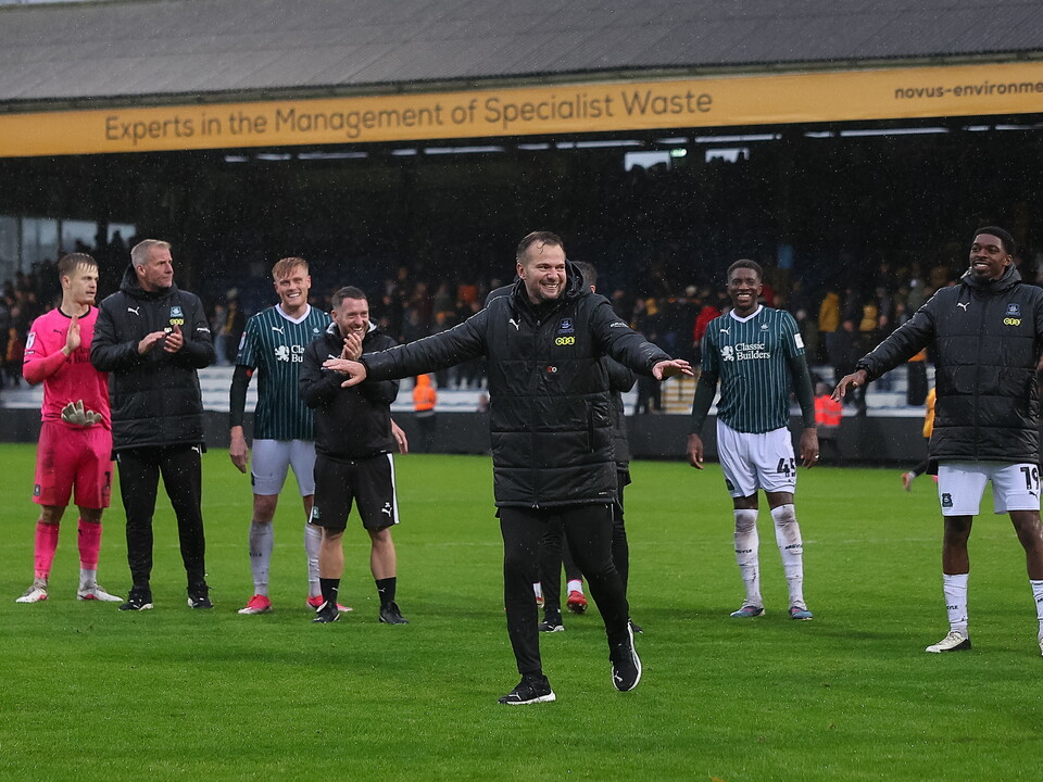 Football manager with arms outstretched on the sideline during a match.