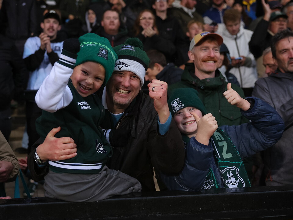 A young boy in a green football shirt hugs a man in a green hat.