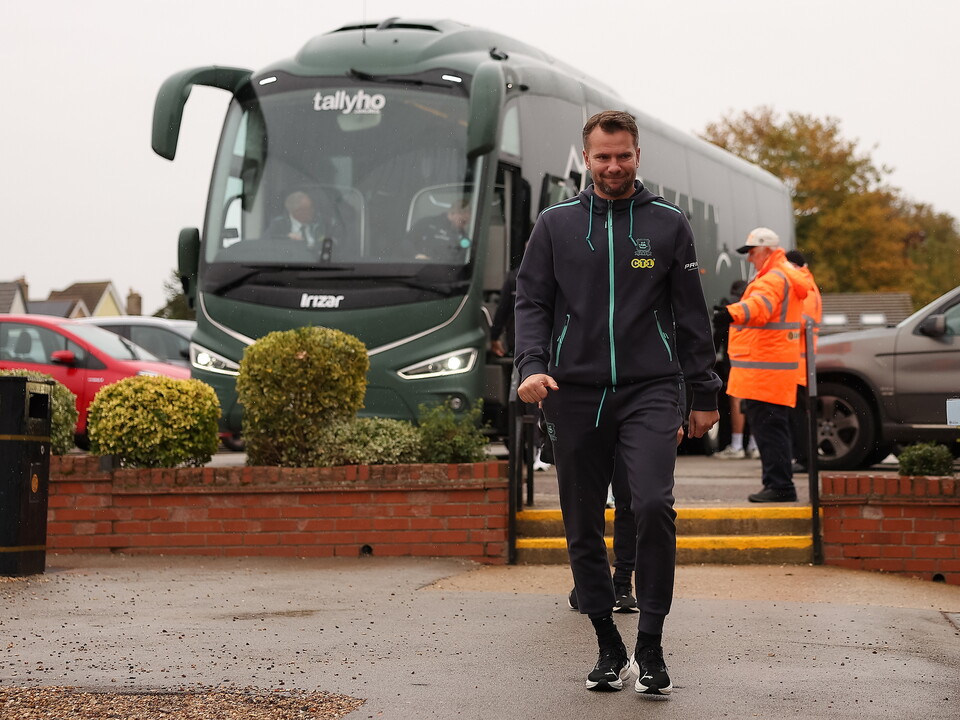 A man in black and blue kit walks in front of a parked coach