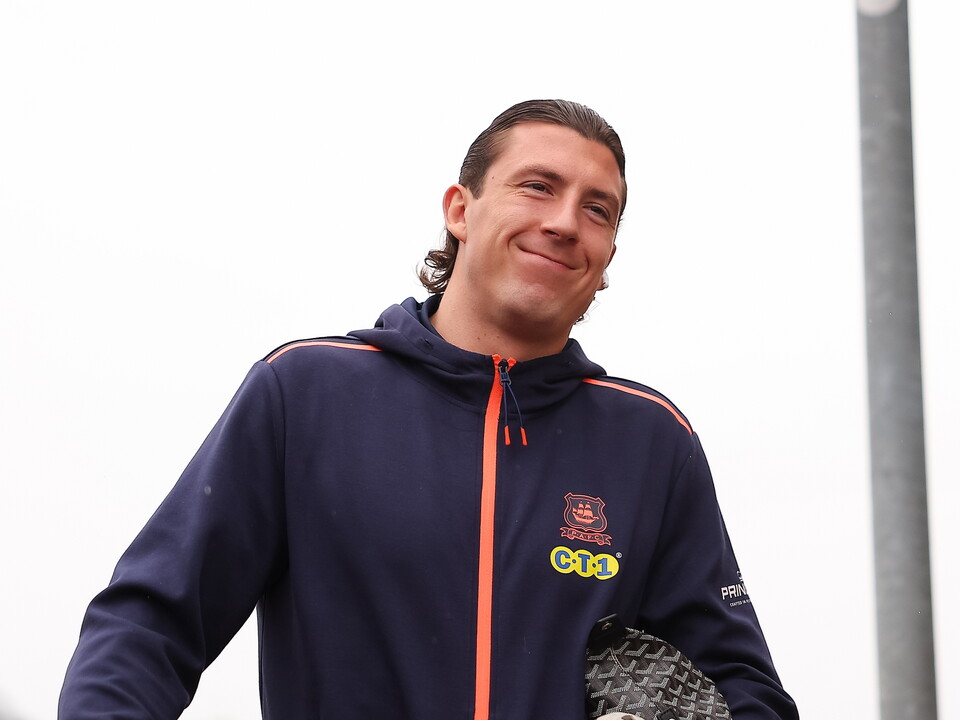 Man in navy blue hoodie with orange stripe and logo holds racket