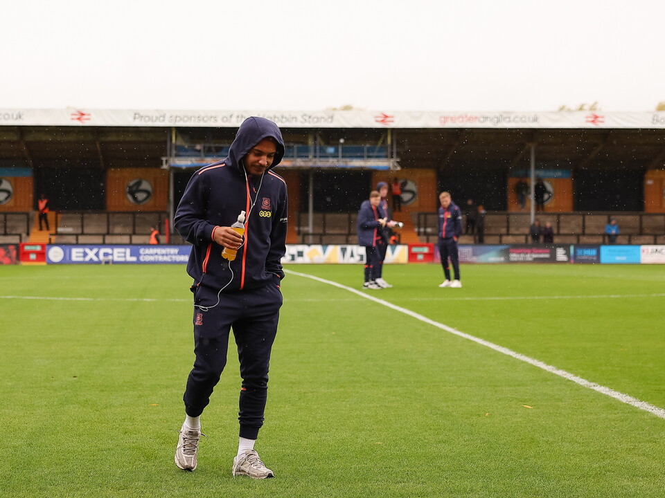 A man in a blue hoodie walks across the field, holding a bottle in his left hand.