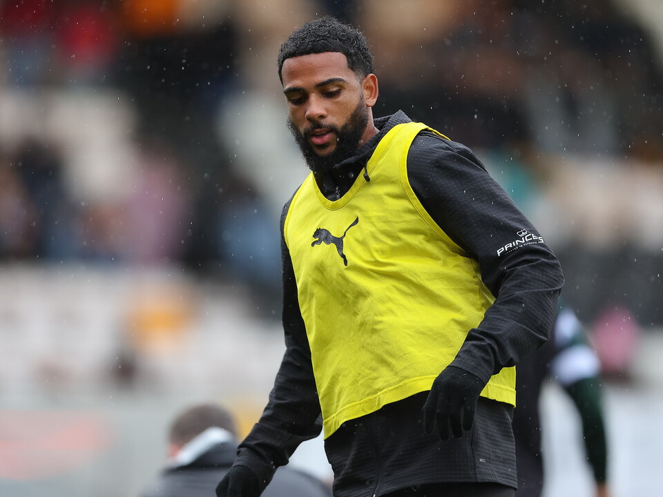 Footballer in yellow vest and black gloves walking in the rain.