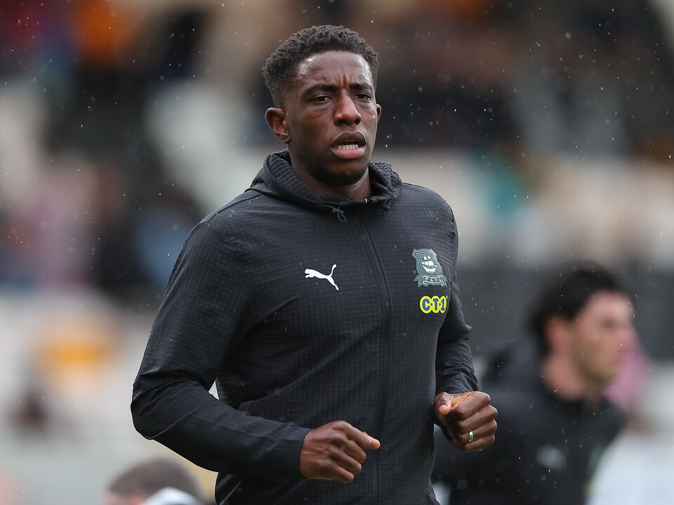 Footballer wearing a black Puma training top running on a pitch in the rain.