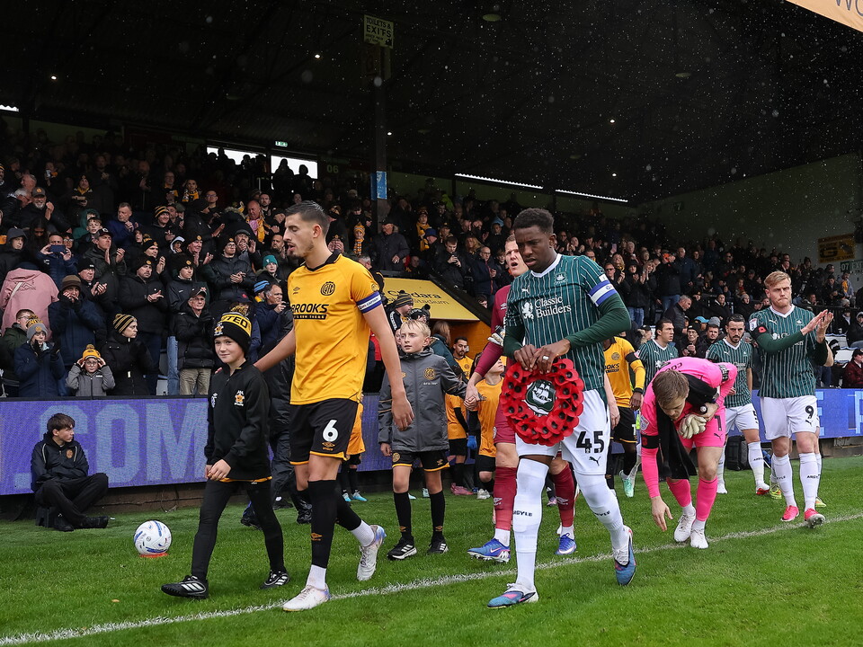 Players walk past a line of poppies during a minute of silence on a rainy football pitch.