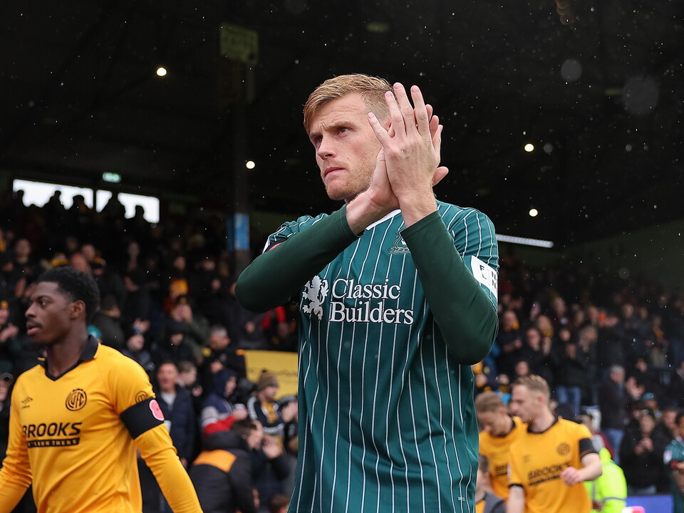 Football player applauding before a crowd, wearing a green shirt with Classic Builders on the front.