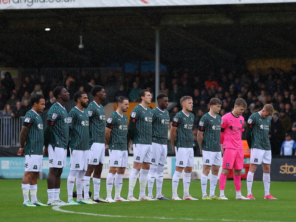 Football team standing on pitch in green and white kits during a match.