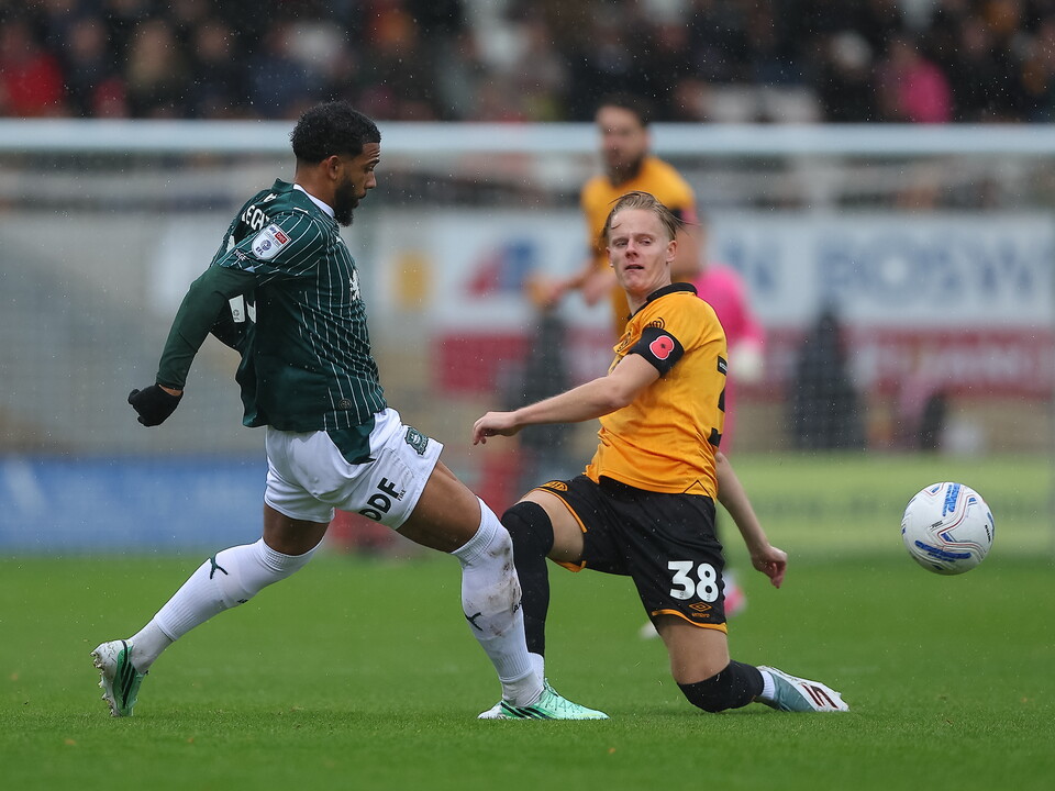 Two football players on a field. One wears green and white, the other, yellow and black. The player in yellow is defending the ball.