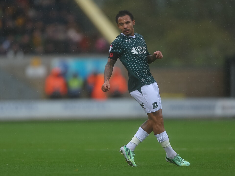 Footballer running on pitch in green and white strip, stadium background.