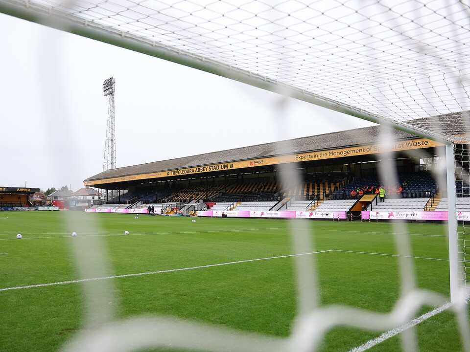 Empty football stadium viewed from behind a net with a small tower in the background