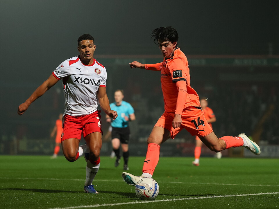 Two players compete for the football on a pitch under the floodlights.