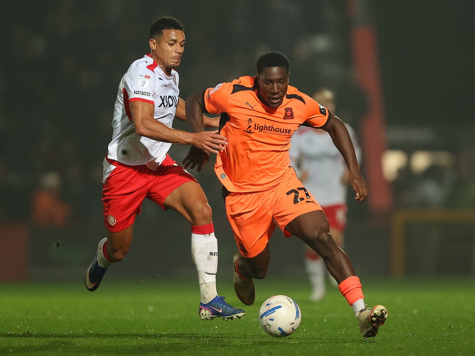 Two players in orange and white, the one in orange wearing number 27, battle for a soccer ball.