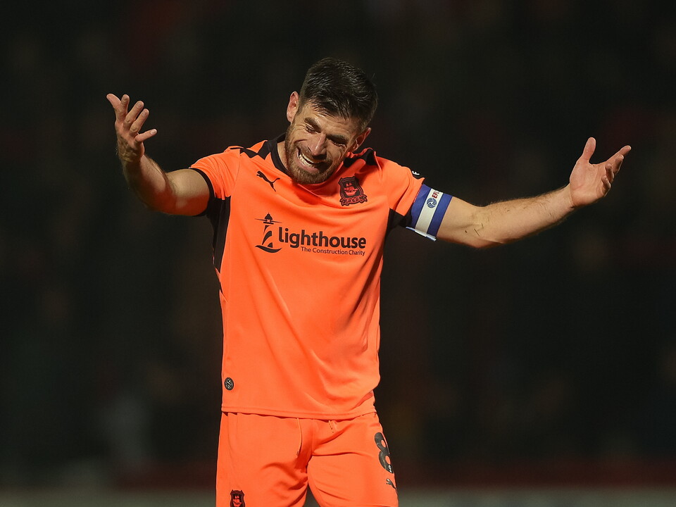 Player in orange kit celebrates with arms outstretched, grinning at the crowd.