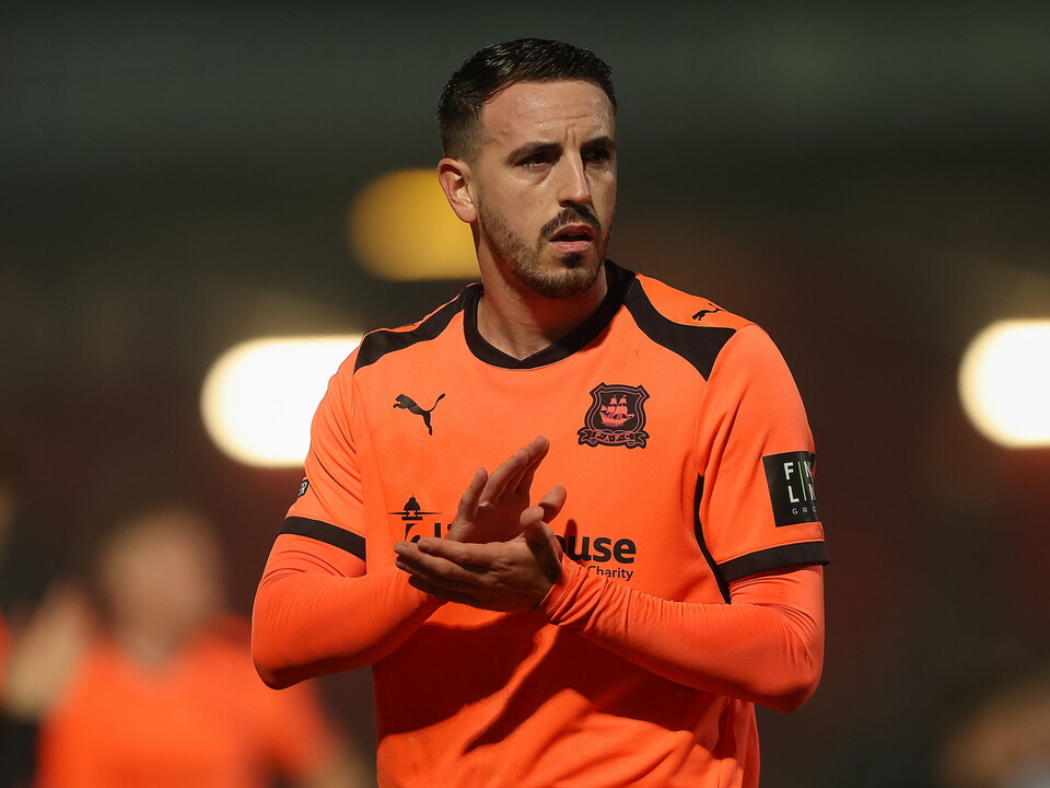 Football player clapping hands in orange jersey with blurred background.