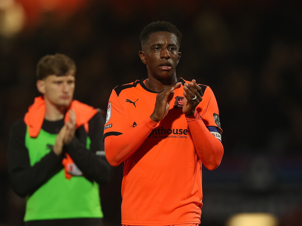 Football player in orange applauds while another in green and black looks on.