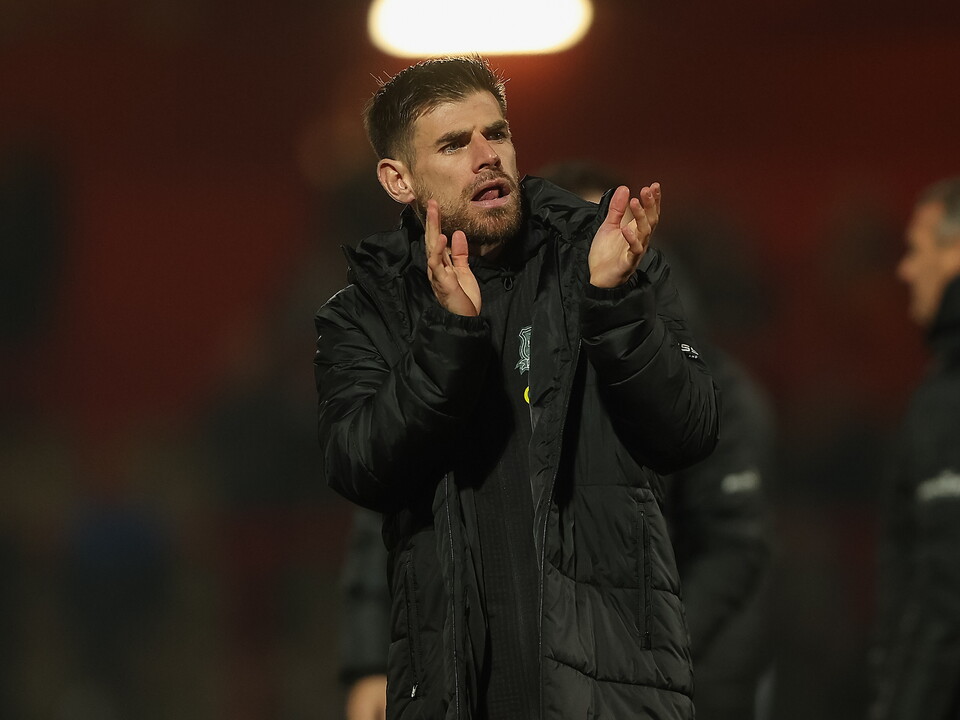 A football coach gesturing with his hands while wearing a black jacket on a field