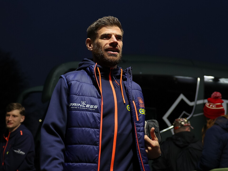 A man in a navy blue jacket with orange stripes stands outdoors at night, holding a smartphone.