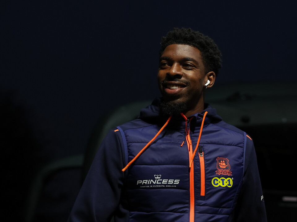Man in blue jacket with orange zippers and a red logo, smiling for a photo.