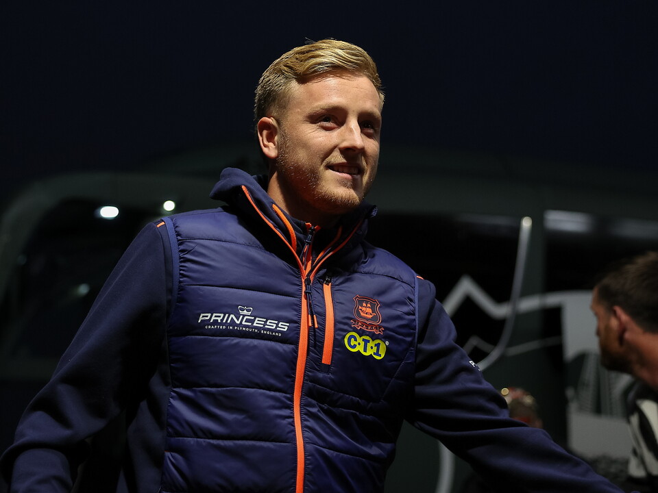 Football player wearing blue jacket with orange zippers stands outside at night