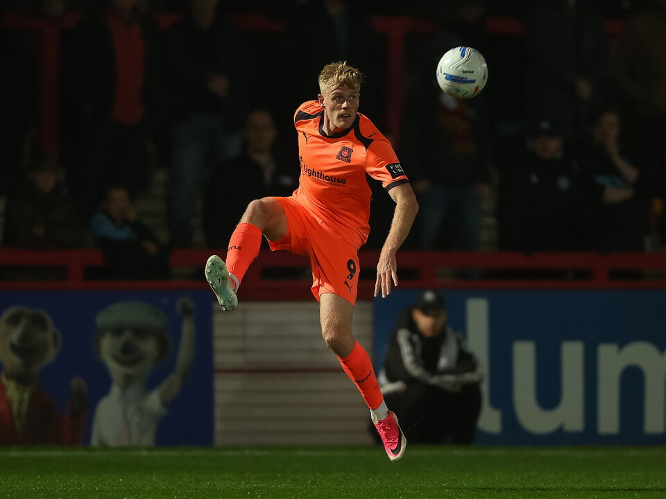 Footballer in orange kit jumps to head ball in air towards goal