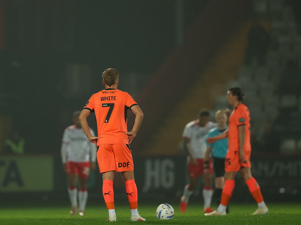 Players in orange kits standing on a pitch, number 7 with hands on hips