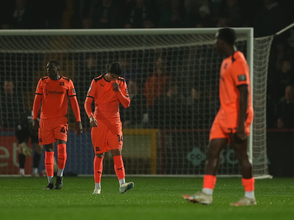 Three football players in orange kits walk towards a goal with a net behind them.