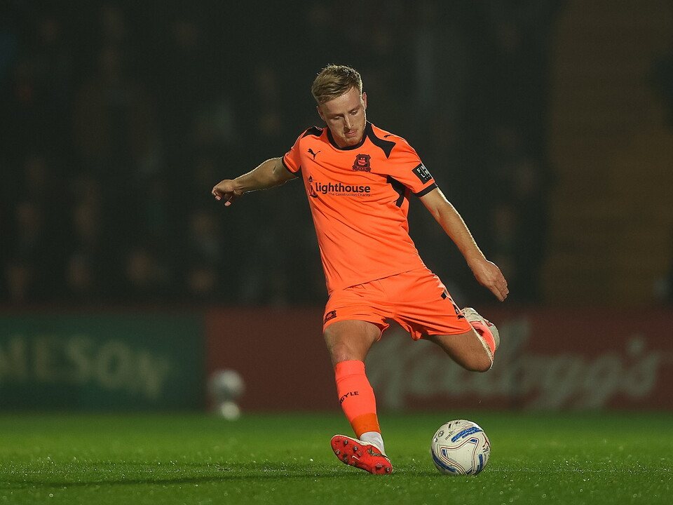 Soccer player in orange kit kicking ball on pitch at night