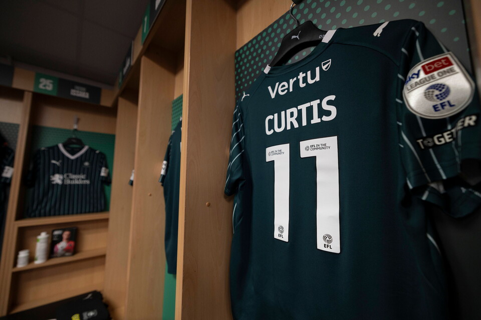 Dark green football shirt with the name Curtis and number 11 hanging in a locker room.