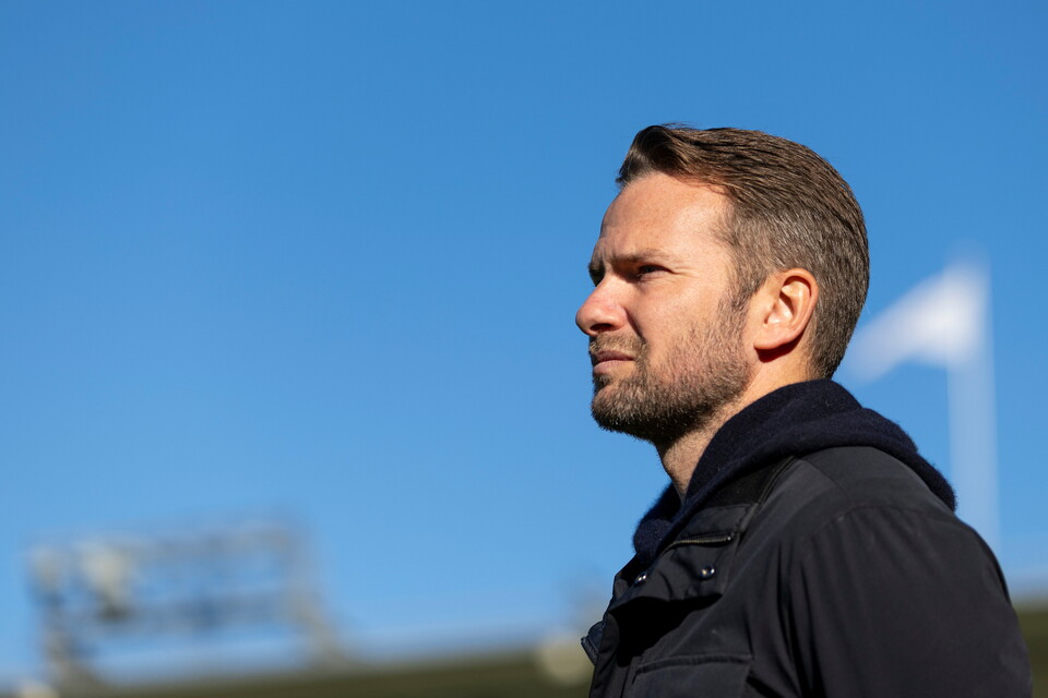 Man in black hoodie standing against blue sky with stadium in background