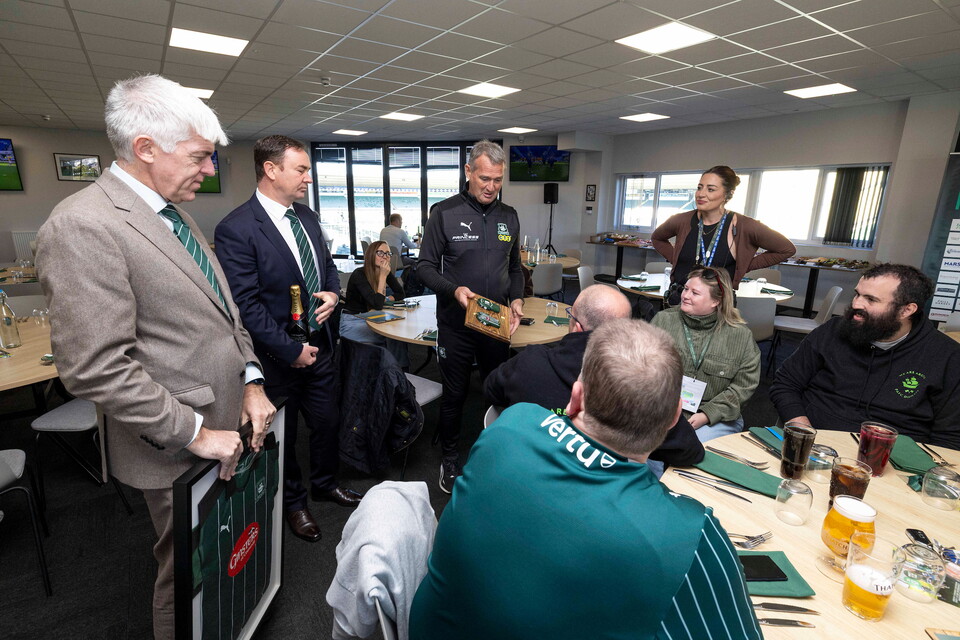 A group of men in suits and jerseys gather in a meeting room for a celebration.
