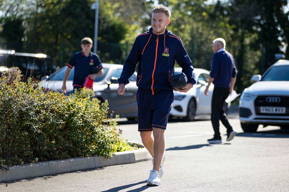 Player walks in blue shirt, shorts and white shoes holding a football helmet