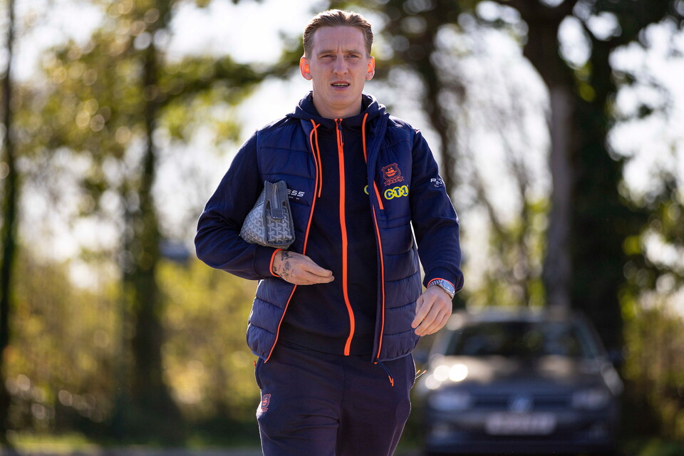 Man in blue jacket running outdoors with a car in the background.
