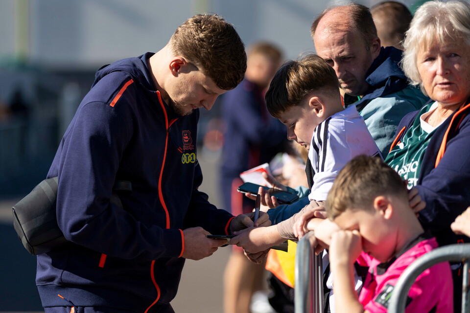 A man signs a football shirt for a boy wearing a pink shirt.