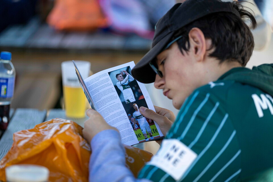 A boy reads a green and white football shirt catalogue at a picnic table.