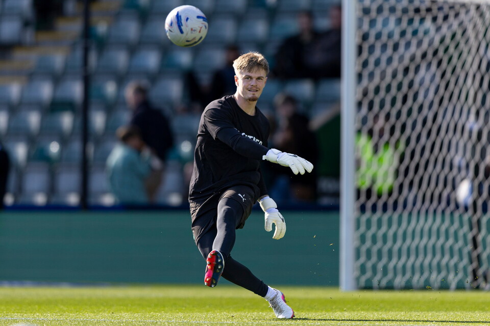 Goalkeeper jumps to catch soccer ball in air with stadium in background.