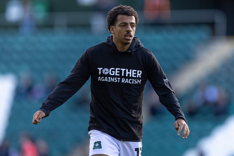 Footballer in black and white kit, walking on pitch, slogan reads "Together Against Racism".