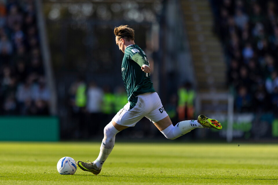 Footballer in green shirt kicks soccer ball on a green pitch.