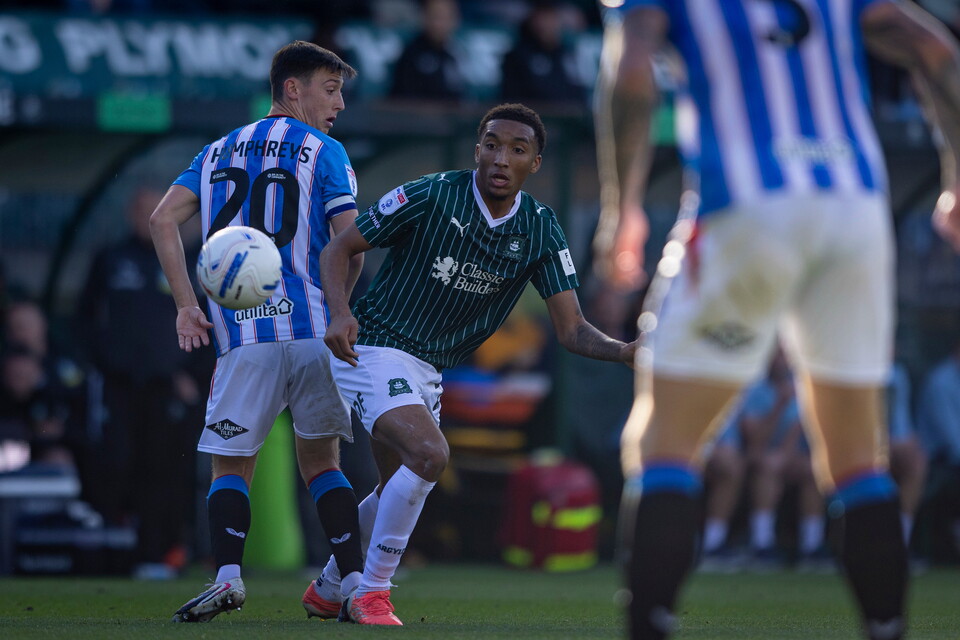 Player number 20 in blue and white plays football with a player in green and white.