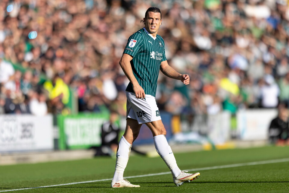Soccer player in green jersey running on green field with large crowd in background