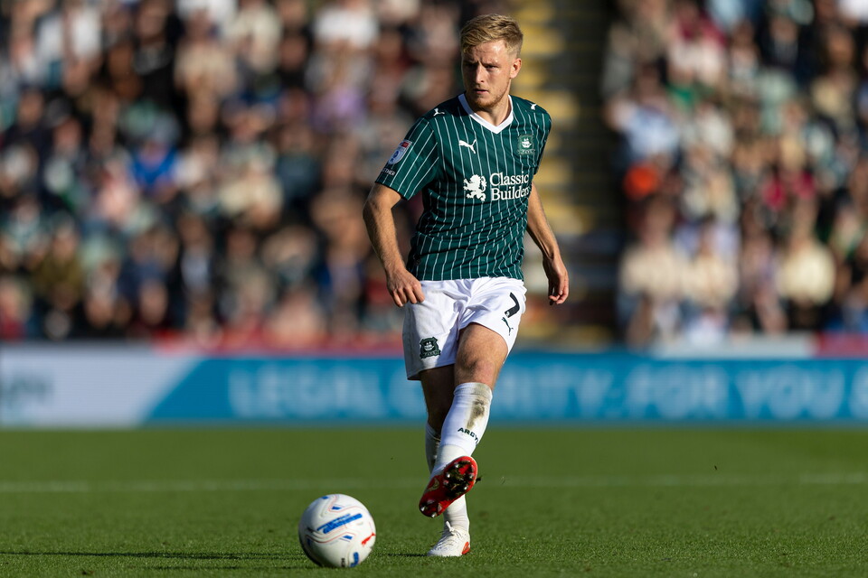 A football player in a green and white kit kicks a ball on the field.
